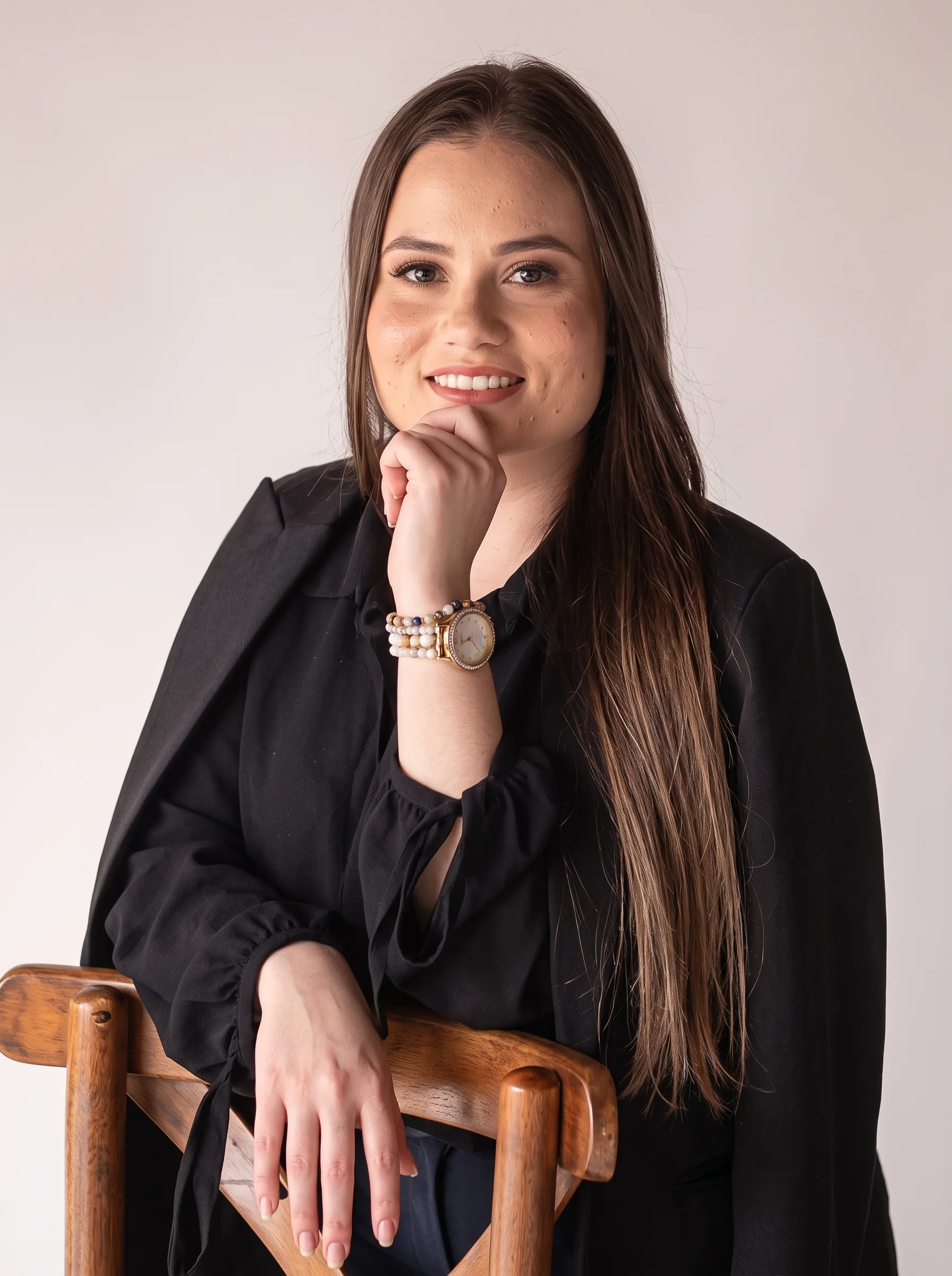 Alana Scalvi, advogada, de blazer preto, sorrindo com a mão no queixo.